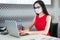 Pretty, young businesslady in red dress, gas mask and glasses sit at the table and work