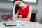 Pretty, young businesslady in red dress and glasses sit at the table and work
