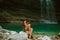 Pretty young crying girl with dark black long hair sitting alone in lagoon of Martvili Canyon, lady in long green cut