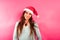 Pretty young girl with freckles and wearing Santa hat, looking at camera relaxed and serene,  on feminine pink background