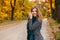 Pretty young happy smiling stylish woman in a trendy gray coat with a checkered green vintage warm scarf walks in the park