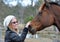 Pretty young happy woman outdoors with pet horse stroking him