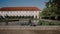 Pretty young lady with backpack sitting on parapet of pond. There are Wallenstein Palace and the pond with fish and