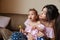 Pretty young mother sitting on sofa with little shocked daughter