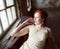 Pretty young red hair woman in old -fashioned style room sitting smiling at window and typing machine, art vintage