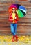 Pretty young smiling woman with colorful umbrella wearing a red leather jacket and rubber boots in autumn over wooden background