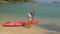 Pretty young sportswoman with sunglasses and swimsuit holds paddle posing near pink plastic canoe on sand beach at