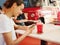 Pretty young tanned woman in white t-shirt is sitting in cafe and uses phone, drinking a cold lemonade or cocktail.