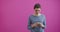 Pretty young teenage girl typing and reading text message on her new modern cell phone mobile on a pink background