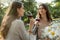 Pretty young two women sitting outdoors in park drinking wine