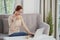 Pretty young Vietnamese woman drinking cup of tea and working on laptop when sitting on sofa at home