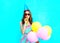 Pretty young woman in a birthday cap blowing a whistle holds an air colorful balloons