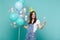 Pretty young woman in birthday hat looking on burning sparkler in hand celebrating holding colorful air balloons