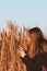 Pretty young woman in black coat with backpack smartphone on pampas grass sunset sky dry reeds Millennial long hair girl