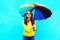 Pretty young woman with colorful umbrella sends air sweet kiss in autumn day over blue background wearing yellow knitted sweater