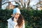 pretty young woman with curly brown hair wears a woollen hat for the cold and covers her face with a dry leaf from a tree. Autumn