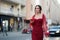 Pretty young woman in an elegant maroon red dress walking with her smartphone