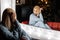 Pretty young woman in a fashion knitted suit is sitting near a vintage mirror with bright lamps in the living room in the evening