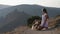 pretty young woman feeding her small chihuahua pet dogs sitting on knees on beautiful sunset mountain landscape