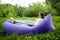 Pretty young woman lying on inflatable sofa lamzac browse in internet on laptop while resting on grass in park