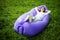 Pretty young woman lying on inflatable sofa lamzac while resting on grass in park on the sun under sky