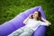 Pretty young woman lying on inflatable sofa lamzac talk on phone while resting on grass in park