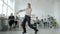 Pretty young woman performing creative modern dance in workplace while colleagues busy with work