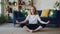 Pretty young woman is practising yoga at home relaxing in simple body position sitting on floor with beautiful furniture