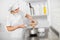 Pretty young woman, professional confectioner, preparing chocolate cream or batter, pouring it from cup to stainless