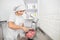 Pretty young woman, professional confectioner, preparing red cream or batter in stainless steel bowl, mixing it with