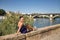 Pretty young woman in a purple suit, sitting on a stone wall by the river, posing happy, Concept beauty, fashion, trend, elegance