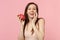 Pretty young woman putting hand on cheek holding fresh ripe pitahaya, dragon fruit isolated on pink pastel wall