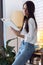 Pretty young woman reading a book while standing in the living room at home