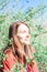 pretty young woman in a red coat is resting in the spring forest among branches with fresh green leaves