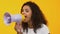 Pretty young woman screaming in megaphone on yellow background, advertisement