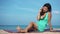 Pretty young woman sitting on beach checking phone. Girl spending vacation with gadget, surrounded by amazing landscape