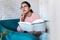 Pretty young woman talking on mobile phone while reading a book on sofa at home