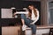 Pretty young woman in a top in jeans in stylish sneakers posing on a table in the kitchen with a modern interior. Trendy beautiful