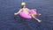 Pretty young woman wearing bikini, yellow hat and purple sunglasses sitting on a pink inflatable ring in swimming pool.