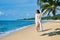 Pretty young woman in white bikini walking barefoot on the sea shore on tropical beach