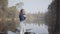 Pretty young woman in white pants, jeans jacket and sunglasses standing on the riverbank. The girl is cold, she rubbing