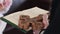 Priest in a black cassock reads a prayer holding a bible with a cross in his hand