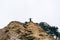 A priest in a black robe stands on a mountain and spreads his arms in the shape of a cross