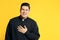 Priest in cassock with clerical collar laughing on yellow. Space for text