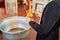 A priest holds candles in hands near the baptismal font.