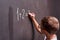 Primary education. Rear view of a schoolboy solves a mathematical example on a blackboard in a math class