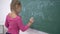 Primary education, schoolgirl with chalk solves examples on mathematics on school green blackboard in class