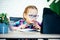 Primary school girl in eyeglasses at the table using her tablet during covid lockdown, distance education for children