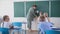 Primary school, little schoolboy with down syndrome learning to write with teacher near blackboard during lesson