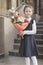 A primary school student in a blue dress stands outdoors and holds a bouquet of flowers